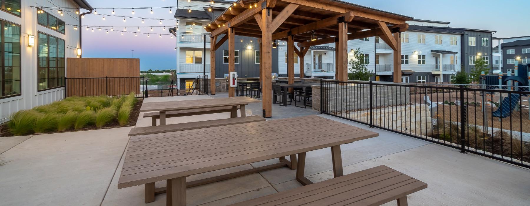 wooden picnic tables on a deck with stringed lighting